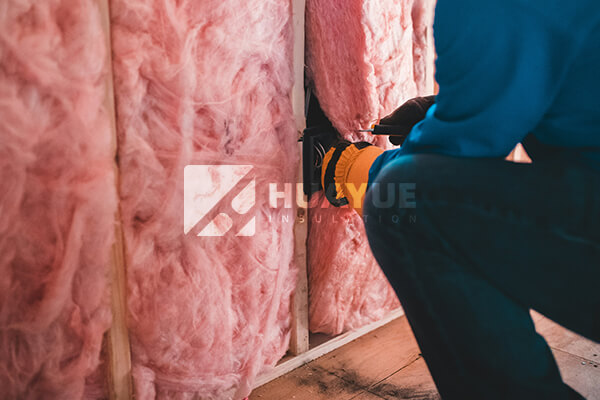 A professional installing fiberglass insulation in a wall cavity